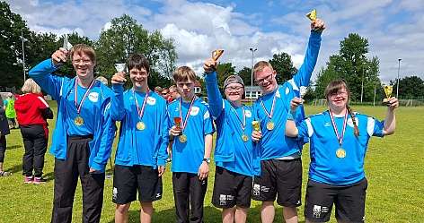 Gruppe von Sportlern in blauen Trikots zeigt stolz ihre Medaillen und Pokale.