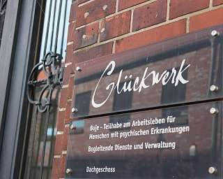 Schild an einer Backsteinmauer mit Informationen zu Glückwerk.