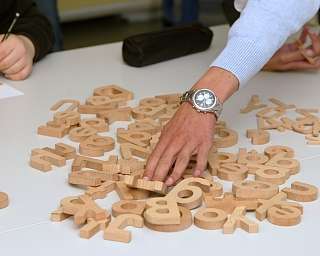Eine Hand greift nach Holzbuchstaben auf einem Tisch.