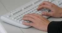 Nahaufnahme von Händen, die auf einer weißen Tastatur tippen.