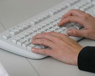 Nahaufnahme von Händen, die auf einer weißen Tastatur tippen.