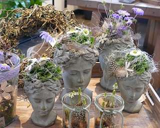 Dekorative Töpfe in Form von Köpfen mit Pflanzen und Blumen.