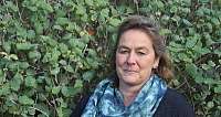 Eine Frau mit einem bunten Schal steht vor einem grünen Busch.