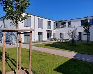 Ansicht einer modernen Wohnanlage mit gepflegtem Garten und Bäumen.